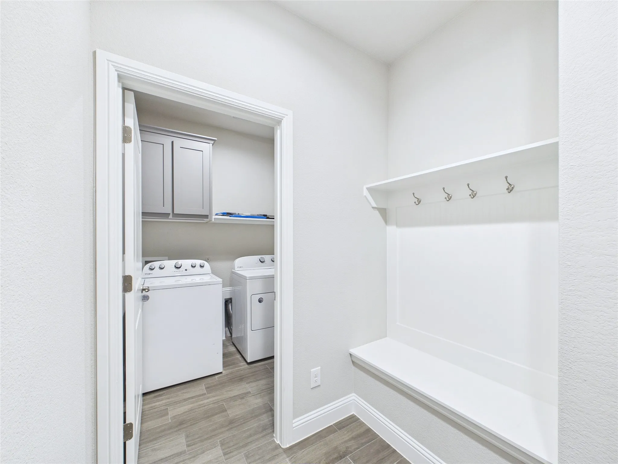 Laundry room entry featuring wood-finish flooring, built-in shelving, and a built-in bench with coat hooks