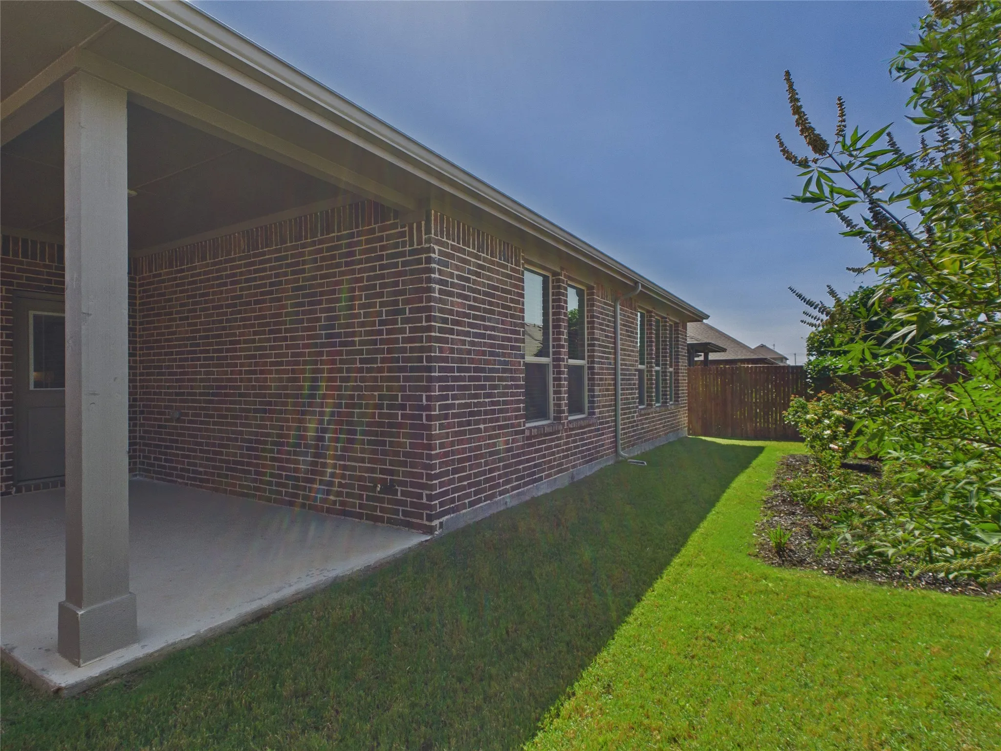 Covered patio with a concrete surface, brick exterior, multiple windows, and a fenced perimeter