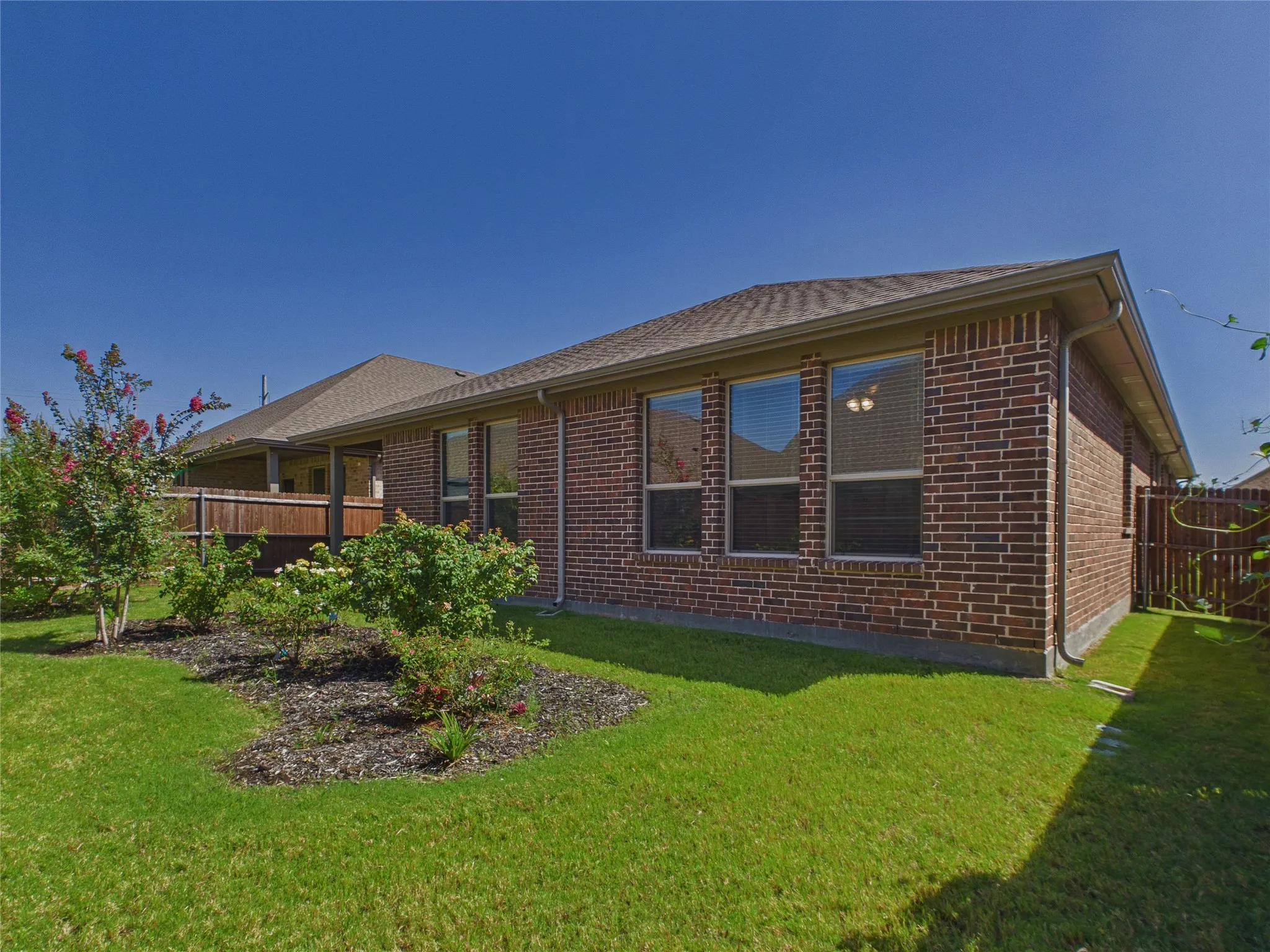 Brick exterior with multiple windows, covered patio, fenced perimeter, and landscaped garden beds