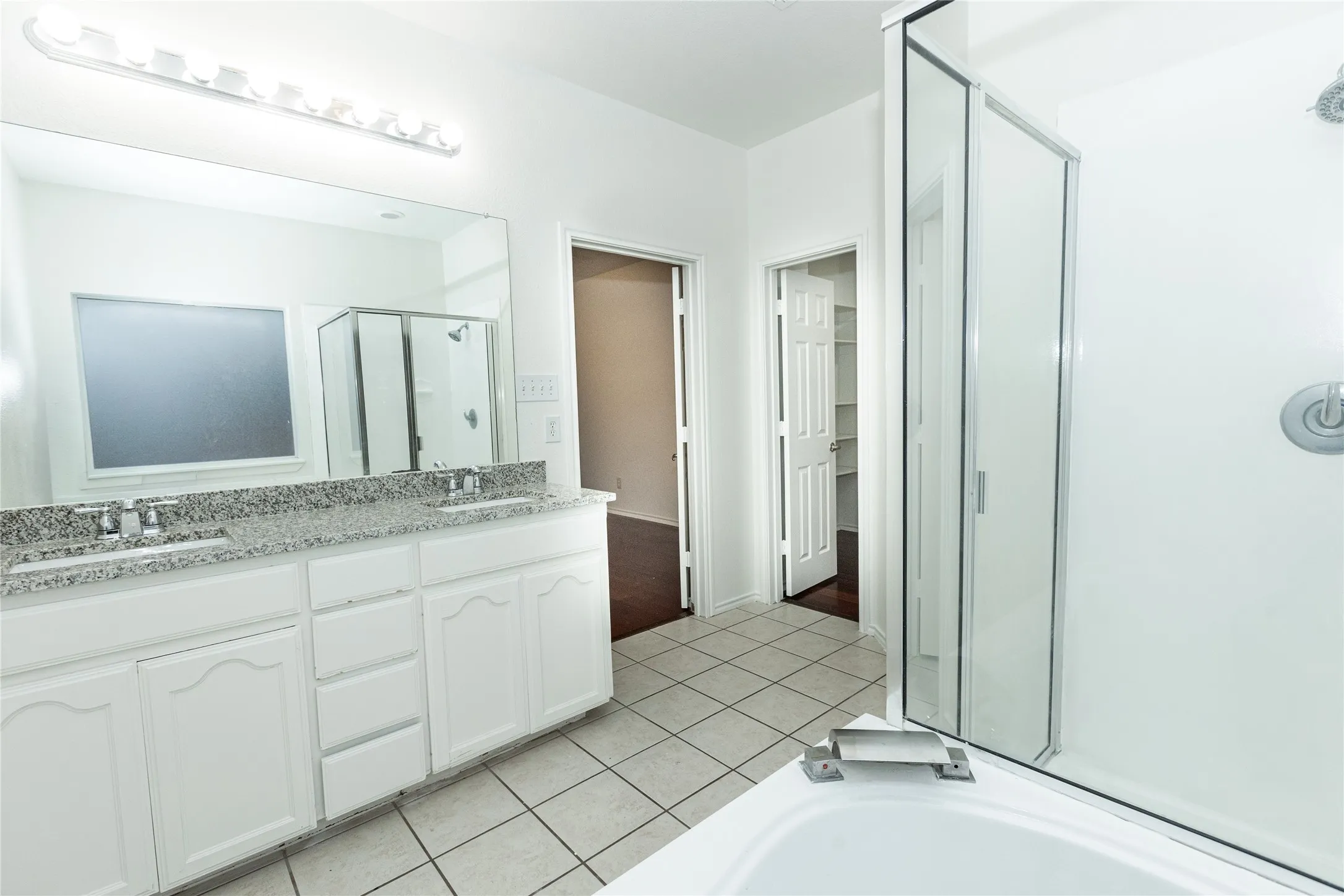 Dual vanity with light-colored speckled countertop, white cabinetry, and large frameless mirror