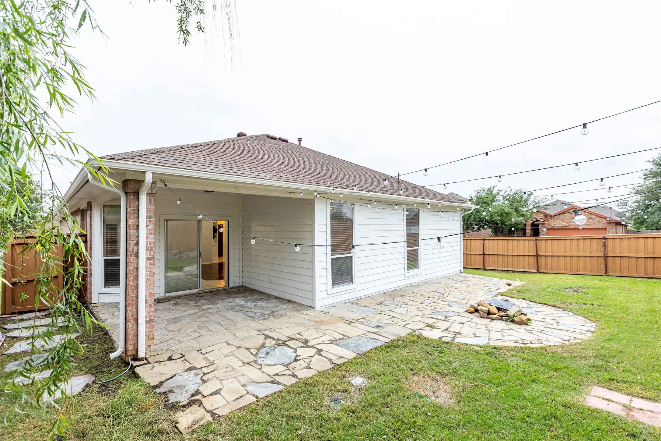 Expansive backyard featuring a covered patio, flagstone hardscaping, a built-in fire pit, a perimeter privacy fence, and a manicured lawn