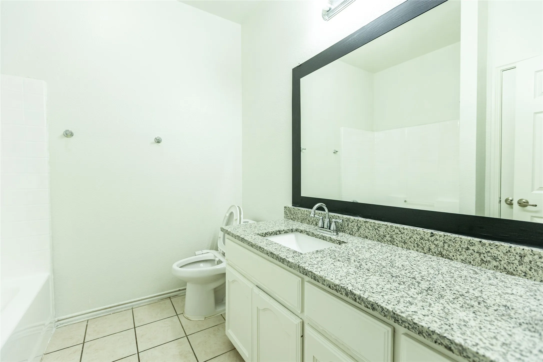 White vanity with an integrated sink, granite countertop, and a large framed mirror