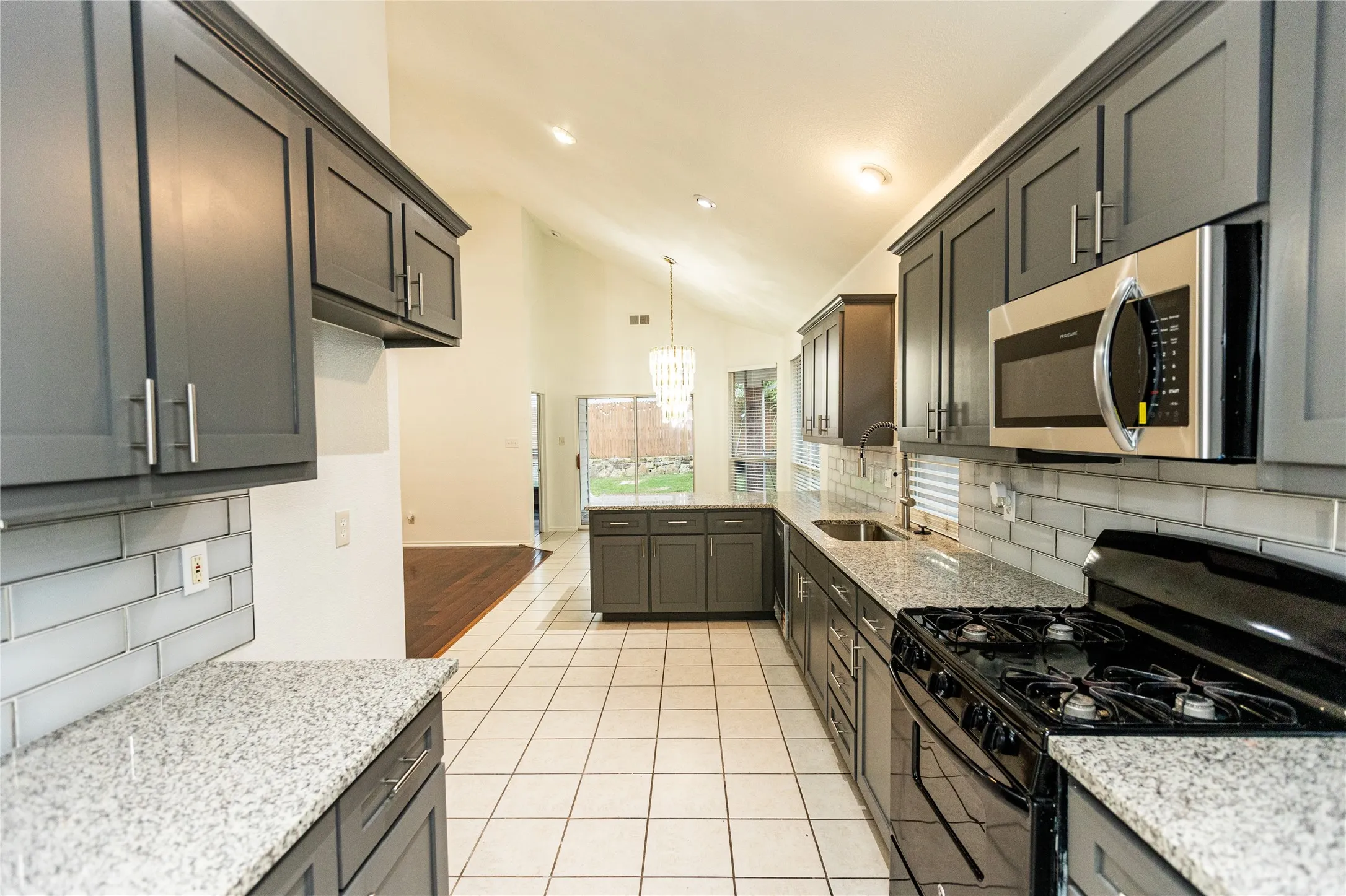 Contemporary kitchen featuring dark cabinetry, light granite countertops, a subway tile backsplash, stainless steel appliances, and tile flooring