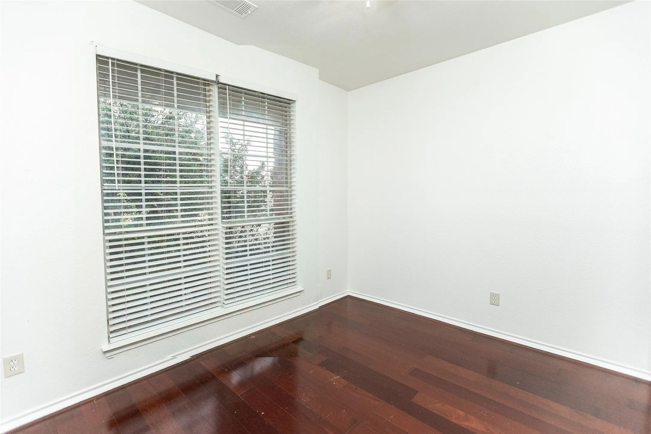 Hardwood flooring, white walls, and a large window with horizontal blinds