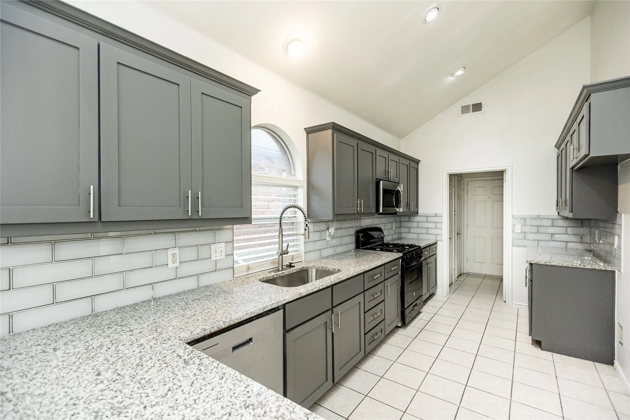 Vaulted ceiling, recessed lighting, white subway tile backsplash, light-toned countertops, and gray cabinetry