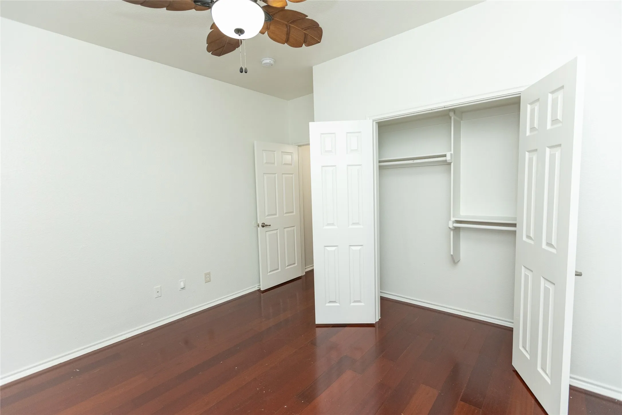 Wood-finish flooring, ceiling fan with light fixture, and a built-in closet with shelving and hanging rods