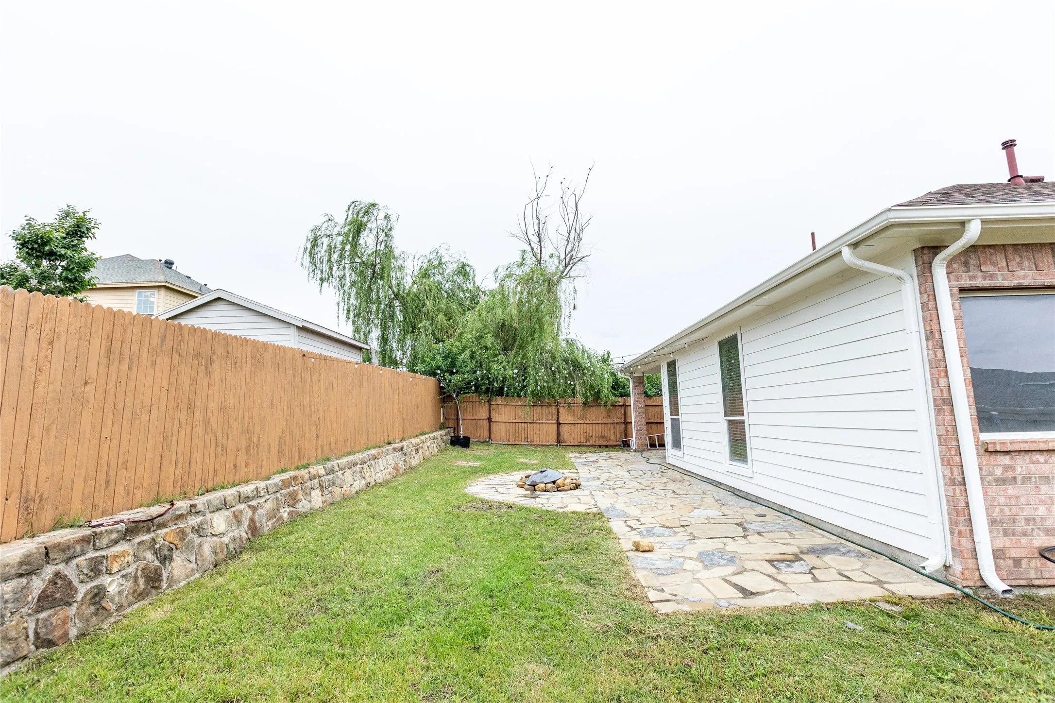 Private backyard with a stone retaining wall, wood fencing, a flagstone patio, and a built-in fire pit