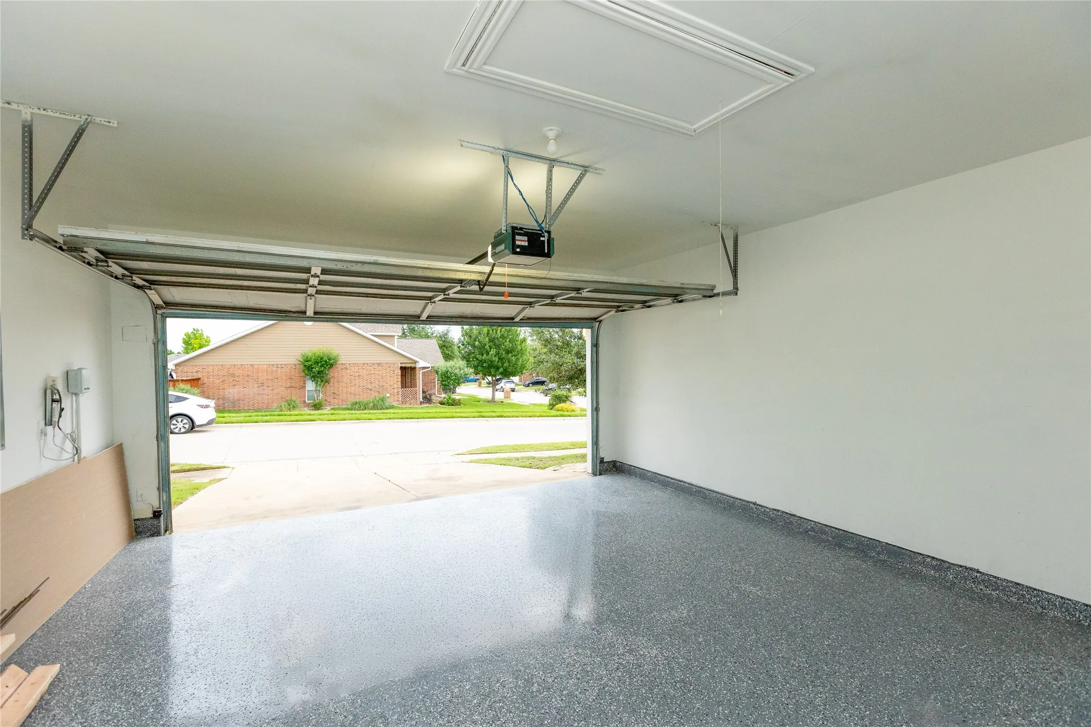 Garage featuring an open overhead door, overhead lighting, an attic access panel, and an epoxy-coated concrete floor
