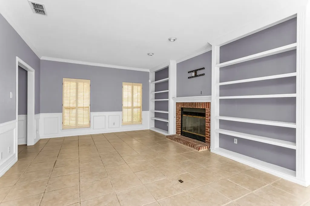 Tile flooring, built-in shelving, brick fireplace, crown molding, and wainscoting