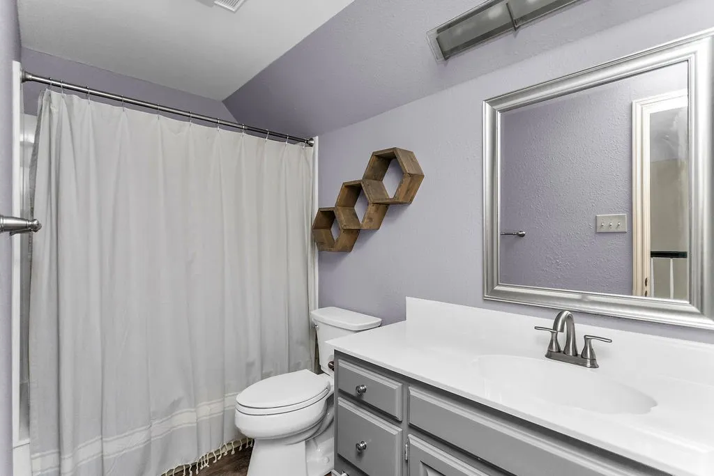 Bathroom featuring a vanity with a white countertop, an undermount sink, brushed nickel fixtures, a framed mirror, and wood-finish flooring