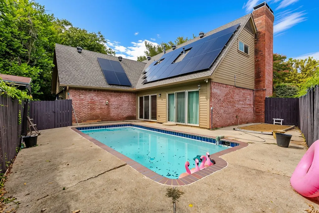 In-ground swimming pool with brick coping, brick exterior with siding, solar panels, and a prominent brick chimney