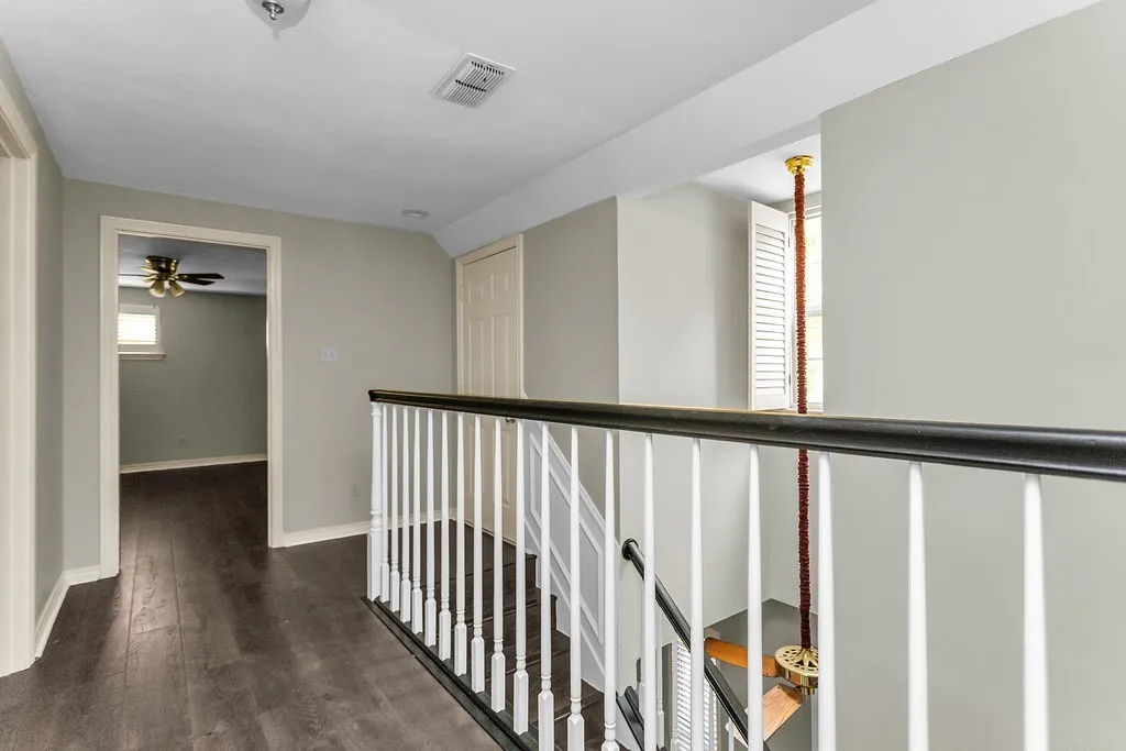Wood-finish flooring, white spindle staircase with dark handrail, neutral wall tones, and recessed lighting