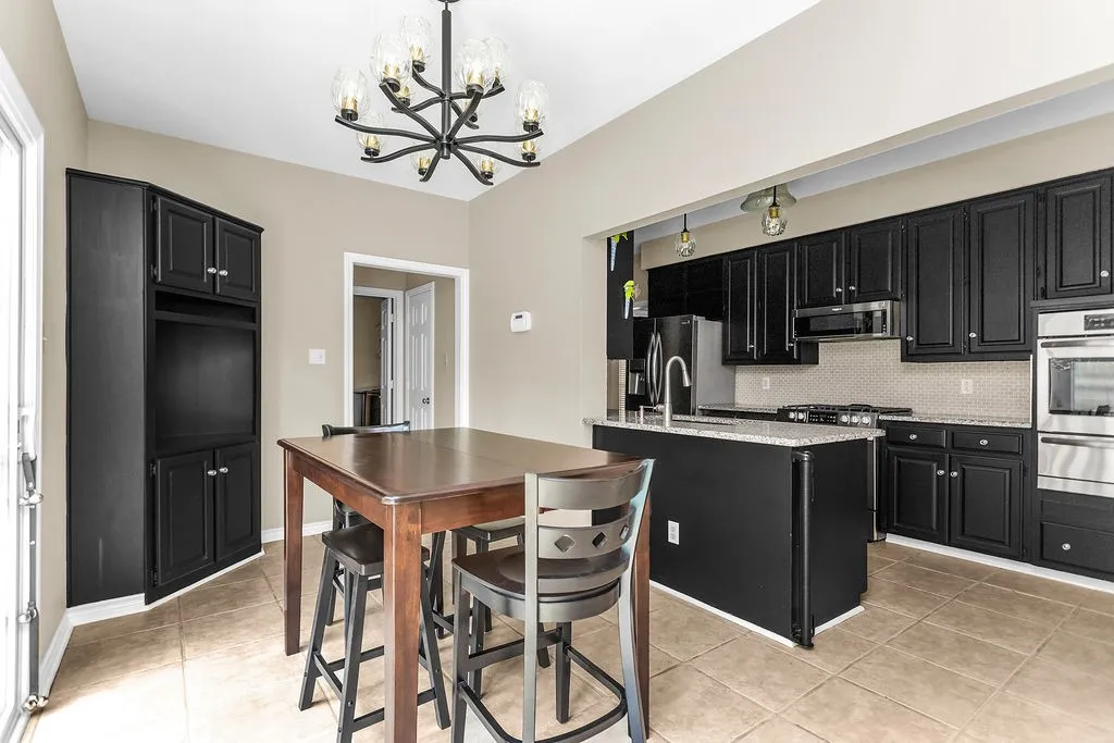 Kitchen featuring black cabinetry, stainless steel appliances, a tiled backsplash, a kitchen island with stone countertops, and tile flooring