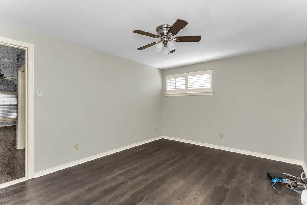 Wood-finish flooring, ceiling fan with integrated lighting, window with plantation shutters, light neutral wall paint, and white trim