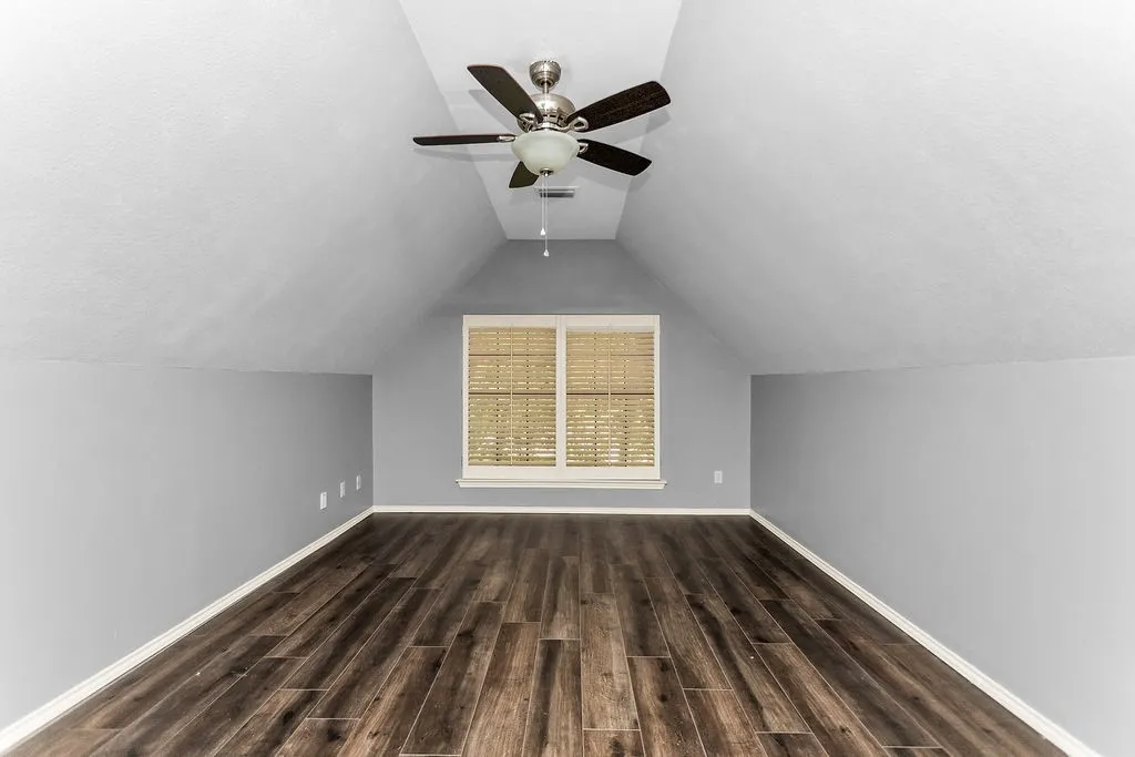 Recessed window with blinds, wood-finish flooring, vaulted ceiling, and ceiling fan with integrated lighting