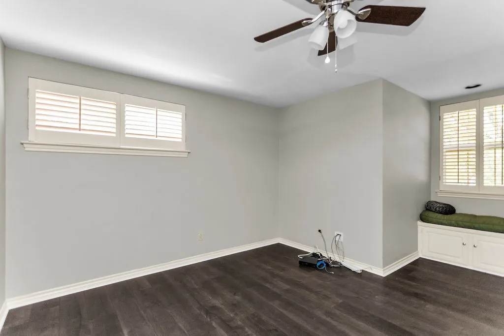 Wood-finish flooring, plantation shutters, ceiling fan with integrated lighting, and built-in window seating with storage