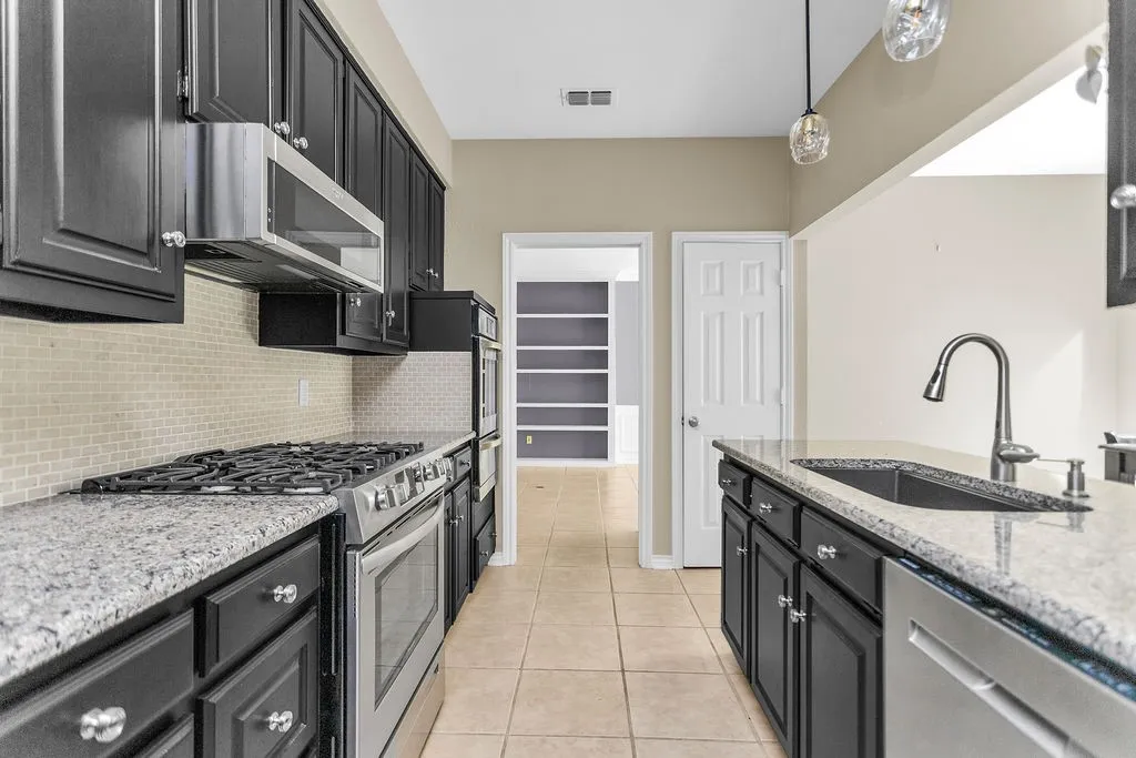 Kitchen featuring dark cabinetry, speckled countertops, stainless steel appliances, a tile backsplash, and tile flooring