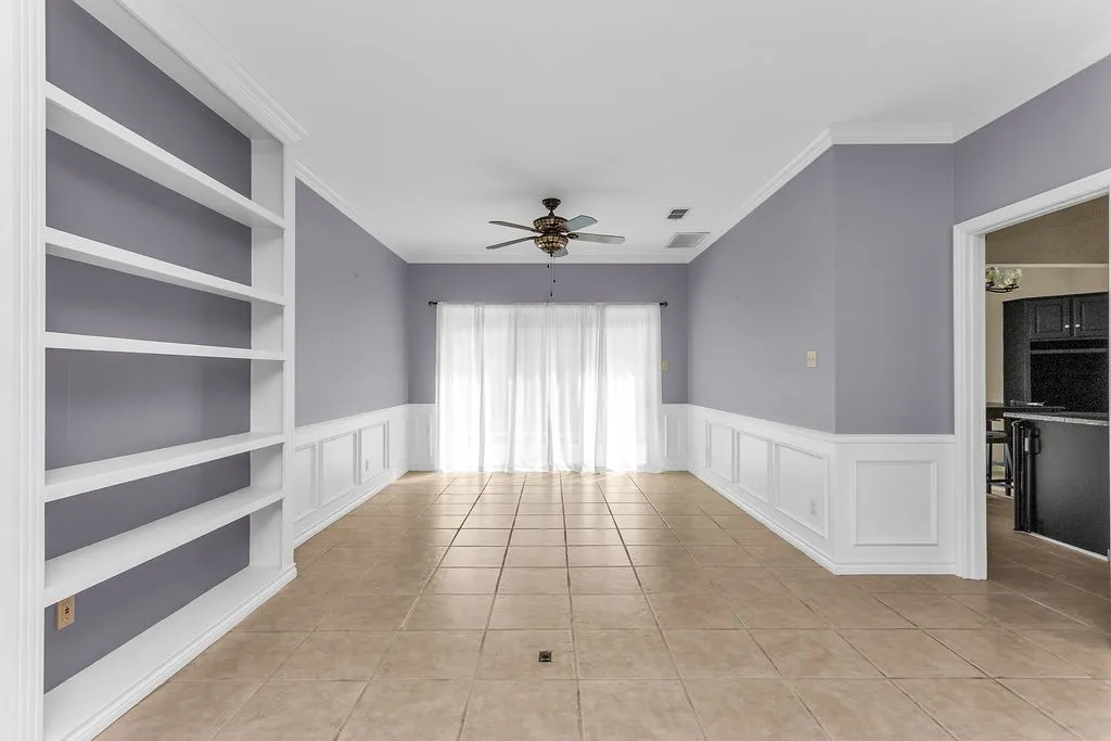 Built-in shelving, tile flooring, ceiling fan, wainscoting, and crown molding