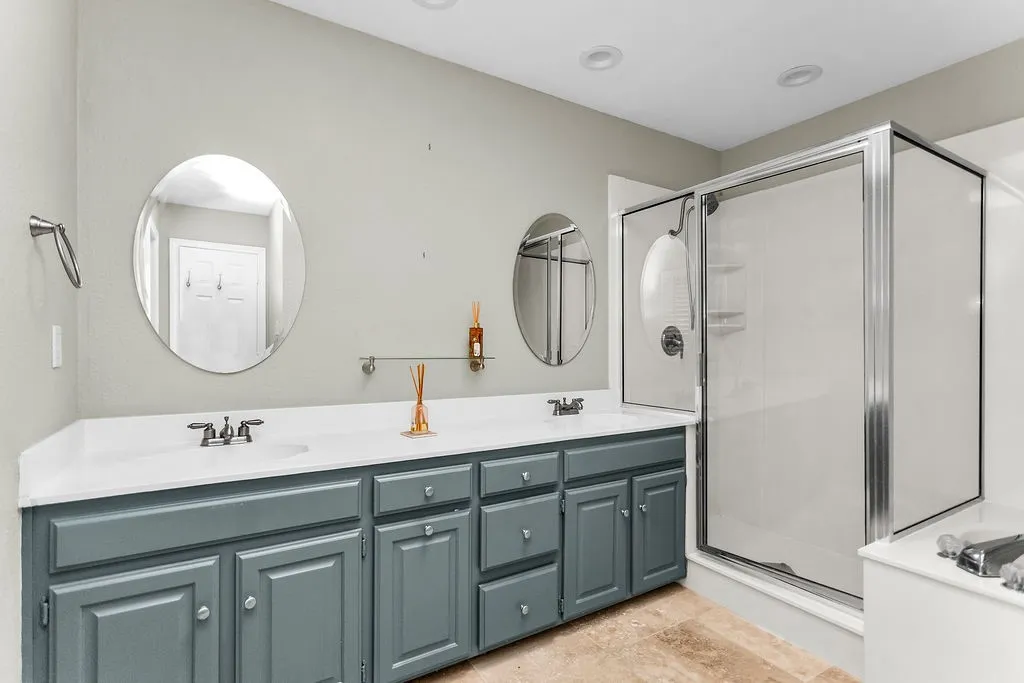 Dual vanity with undermount sinks, white countertop, gray cabinetry, and two oval mirrors