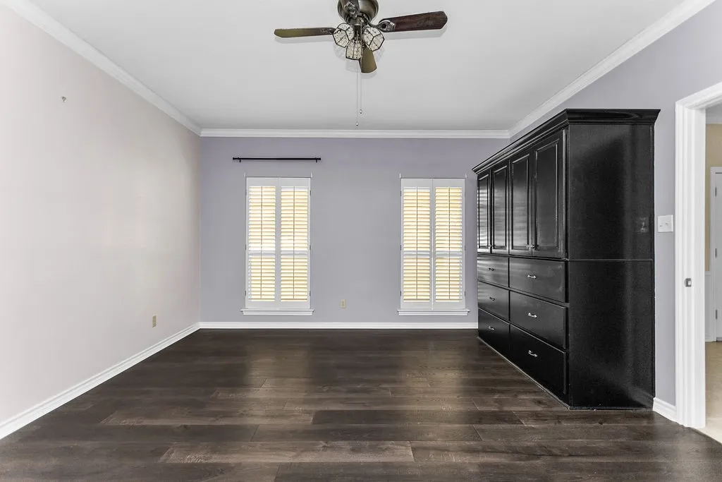 Wood-finish flooring, ceiling fan, crown molding, double windows with plantation shutters, and built-in cabinetry