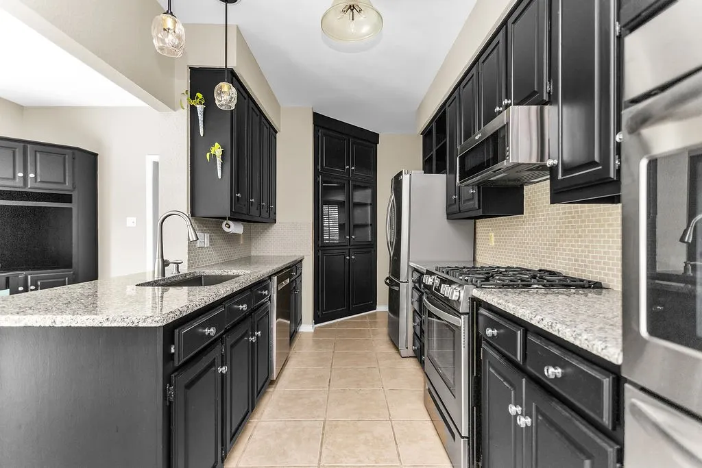 Galley kitchen featuring dark wood cabinetry, light-toned countertops, and stainless steel appliances
