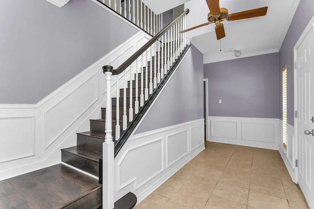 Hardwood staircase, wainscoting, tile flooring, ceiling fan, and crown molding