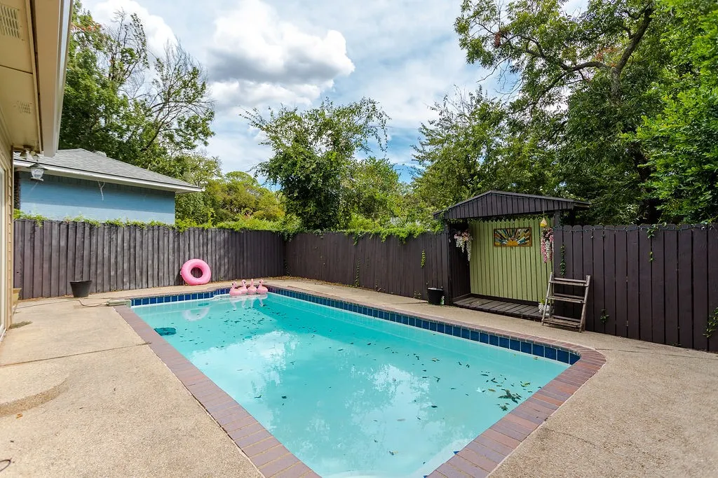 Rectangular swimming pool with concrete decking and brick coping, surrounded by a wood privacy fence