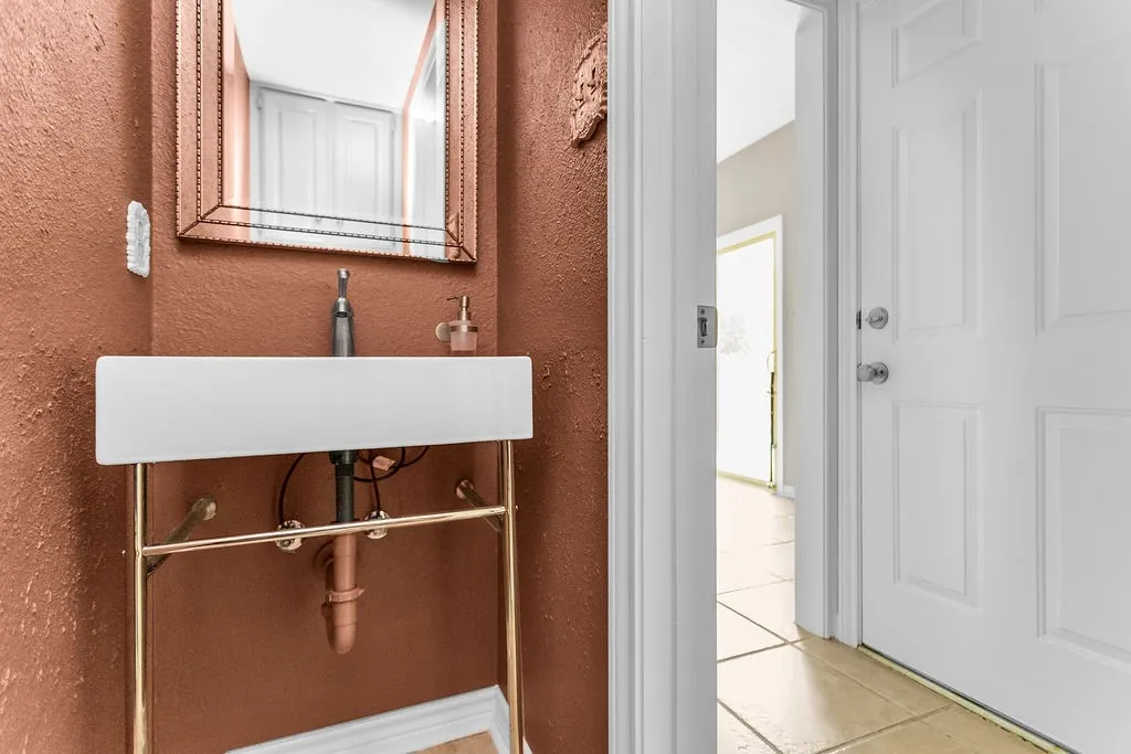 Wall-mounted rectangular sink with gold-tone support frame, textured wall finish, and panel door
