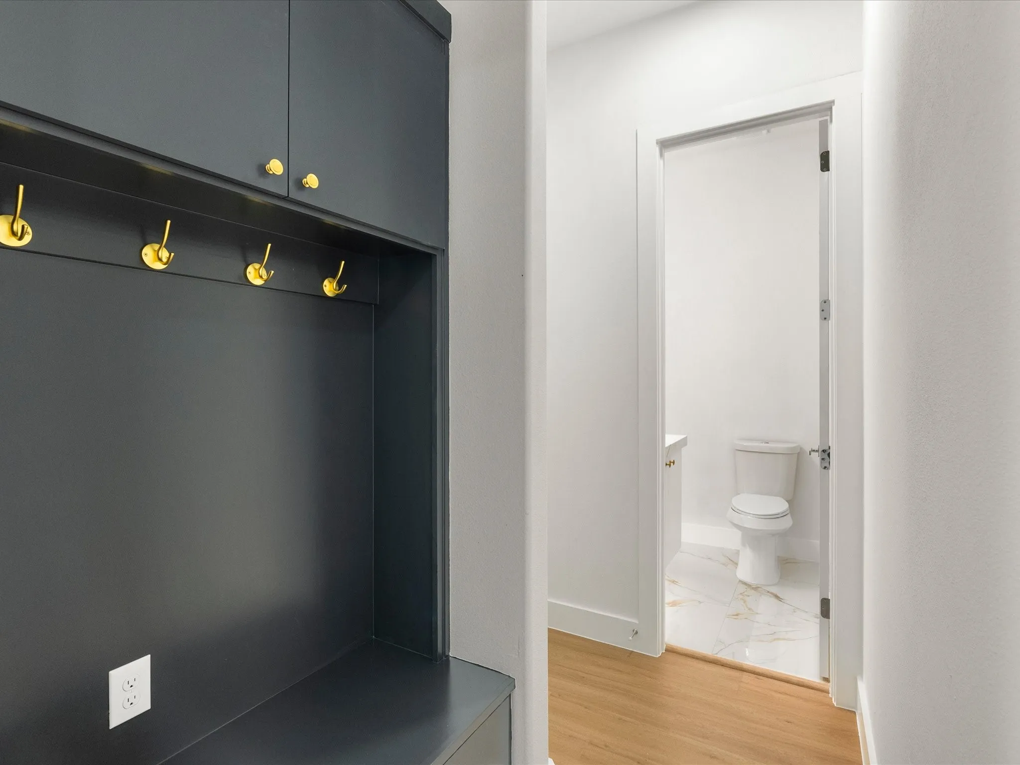 Built-in cabinetry with gold-toned hardware, five gold-toned wall hooks, and a built-in bench