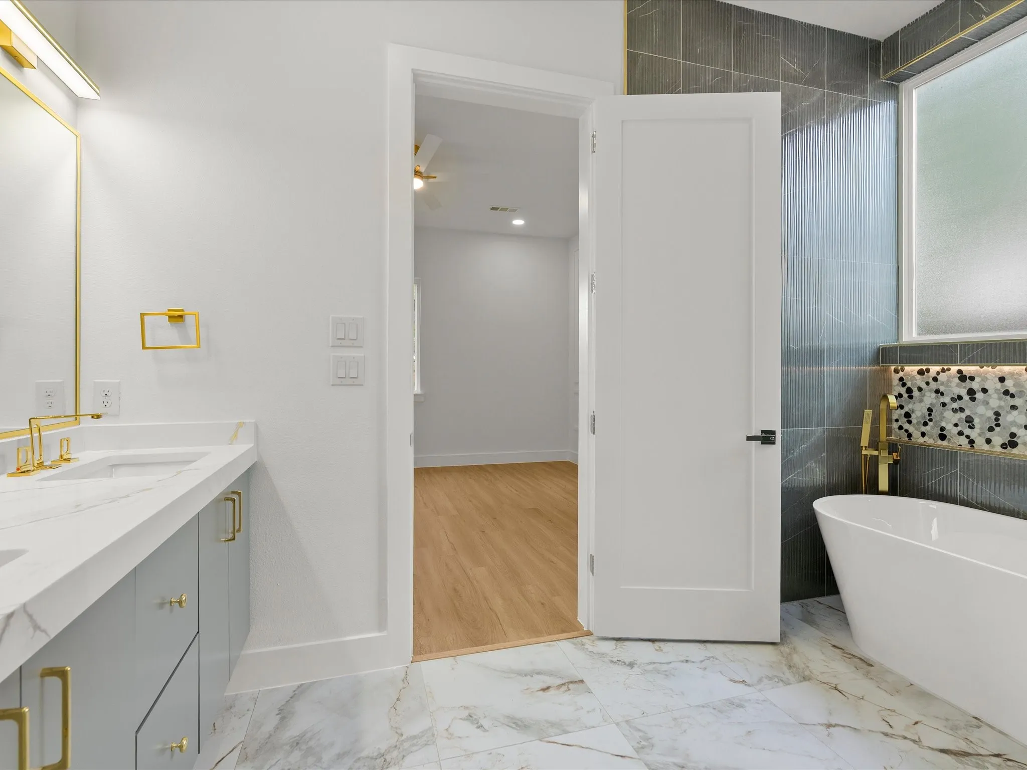 Freestanding soaking tub with gold-tone fixtures, tiled up to the ceiling.