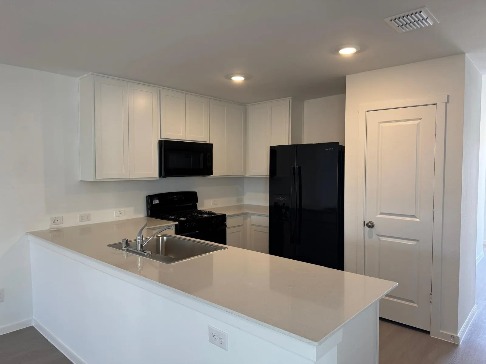 Kitchen with white cabinets, black appliances, a peninsula, dark wood-style floors, and light stone counters