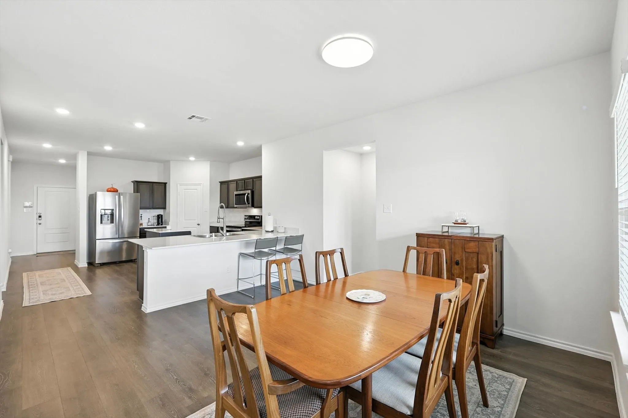Open-concept design featuring wood-finish flooring, a kitchen island with seating, stainless steel appliances, and recessed lighting