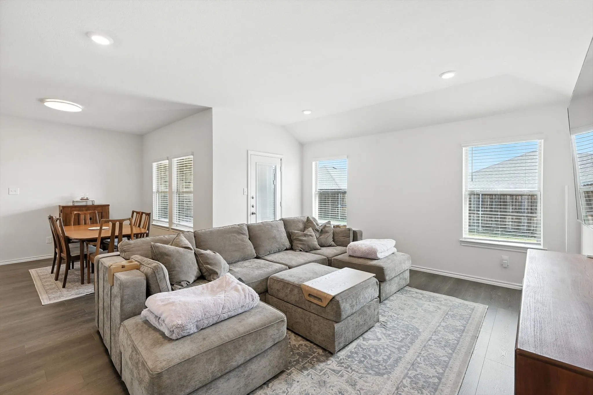 Open-concept living space with wood-finish flooring, recessed lighting, and multiple windows with blinds
