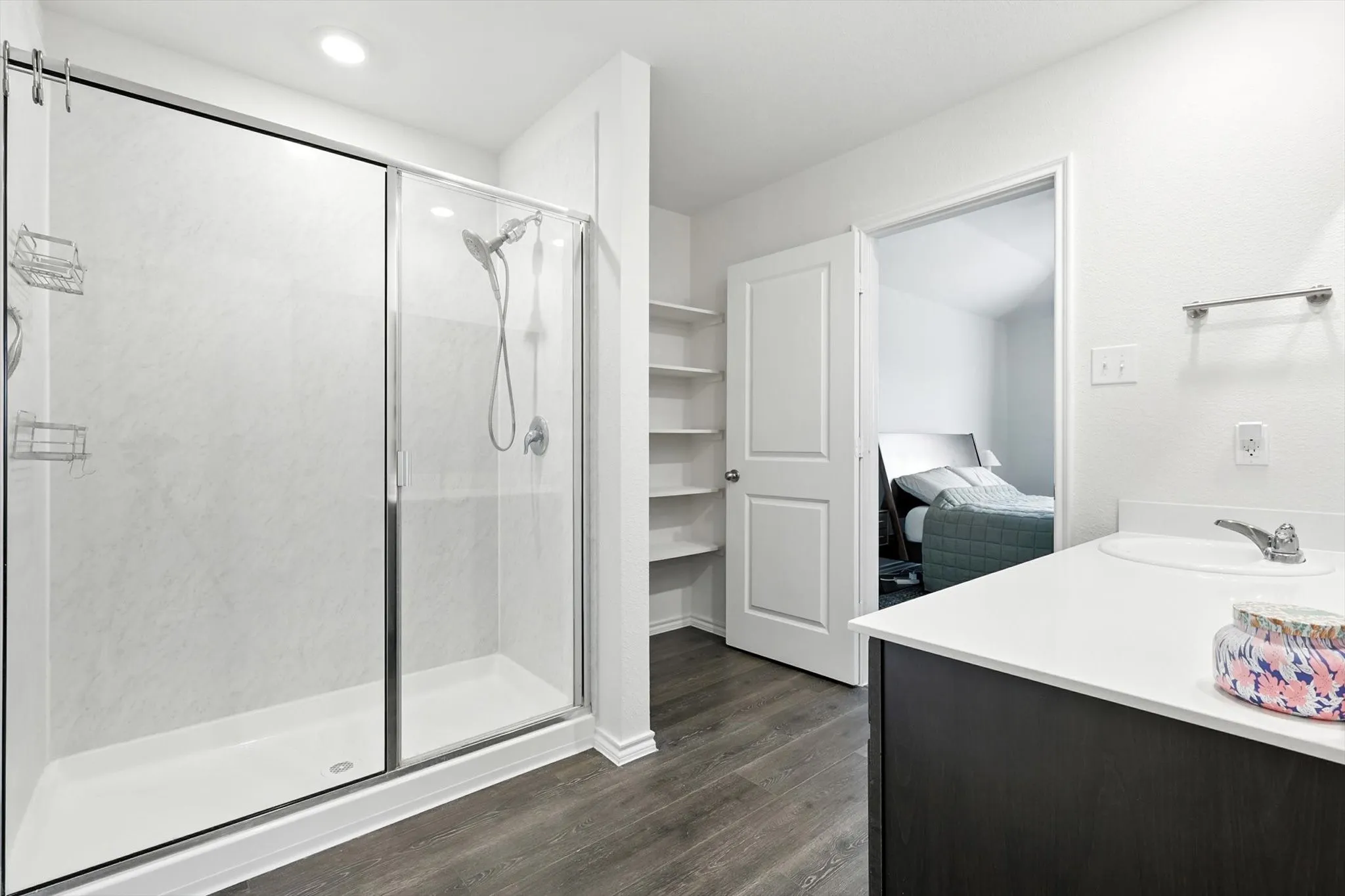 Walk-in shower with sliding glass door, single vanity with integrated sink, wood-finish flooring, and built-in shelving