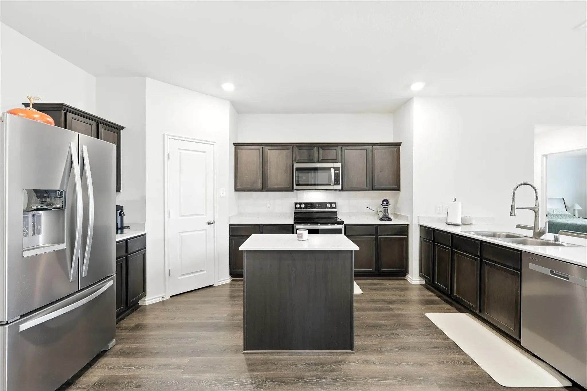Kitchen featuring wood-finish flooring, dark wood cabinetry, a central island, stainless steel appliances, and light-toned countertops
