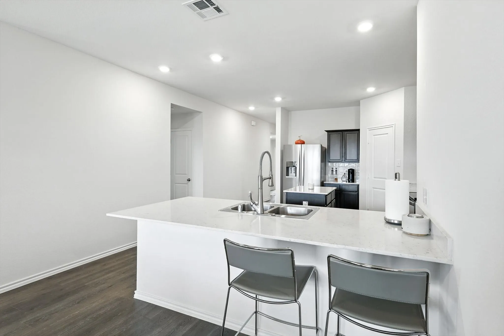 Kitchen island with an undermount dual-basin sink, stainless steel gooseneck faucet, light-toned countertop, recessed lighting, and wood-finish flooring