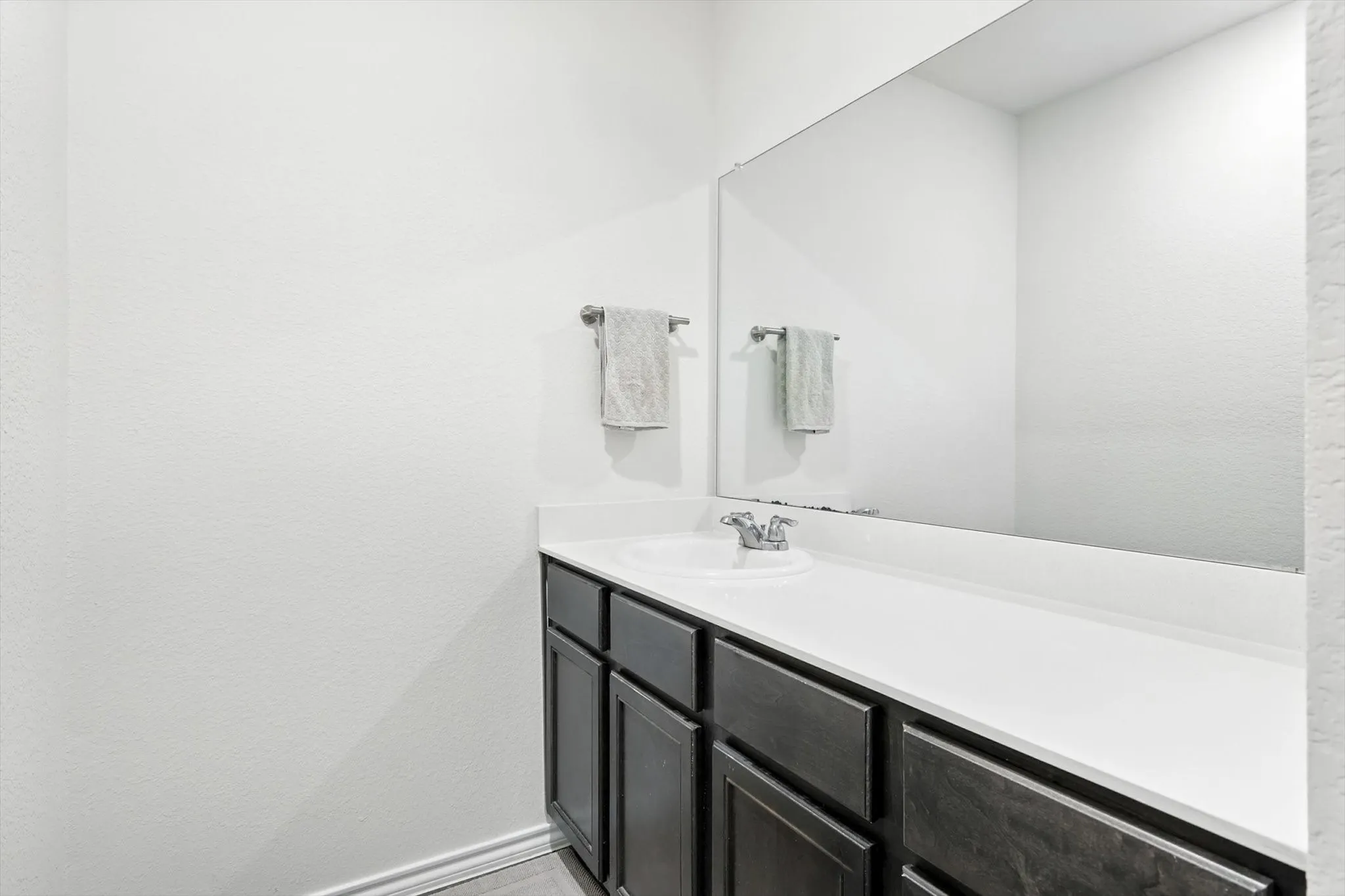 Vanity with dark wood-finish cabinetry, integrated single-basin sink, chrome faucet, and full-width mirror