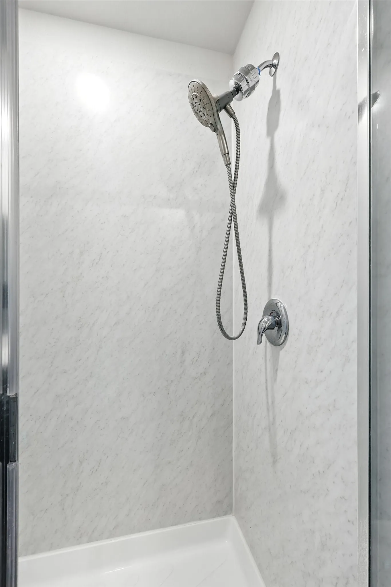 Shower enclosure with textured wall panels, a handheld showerhead, and a separate shower control