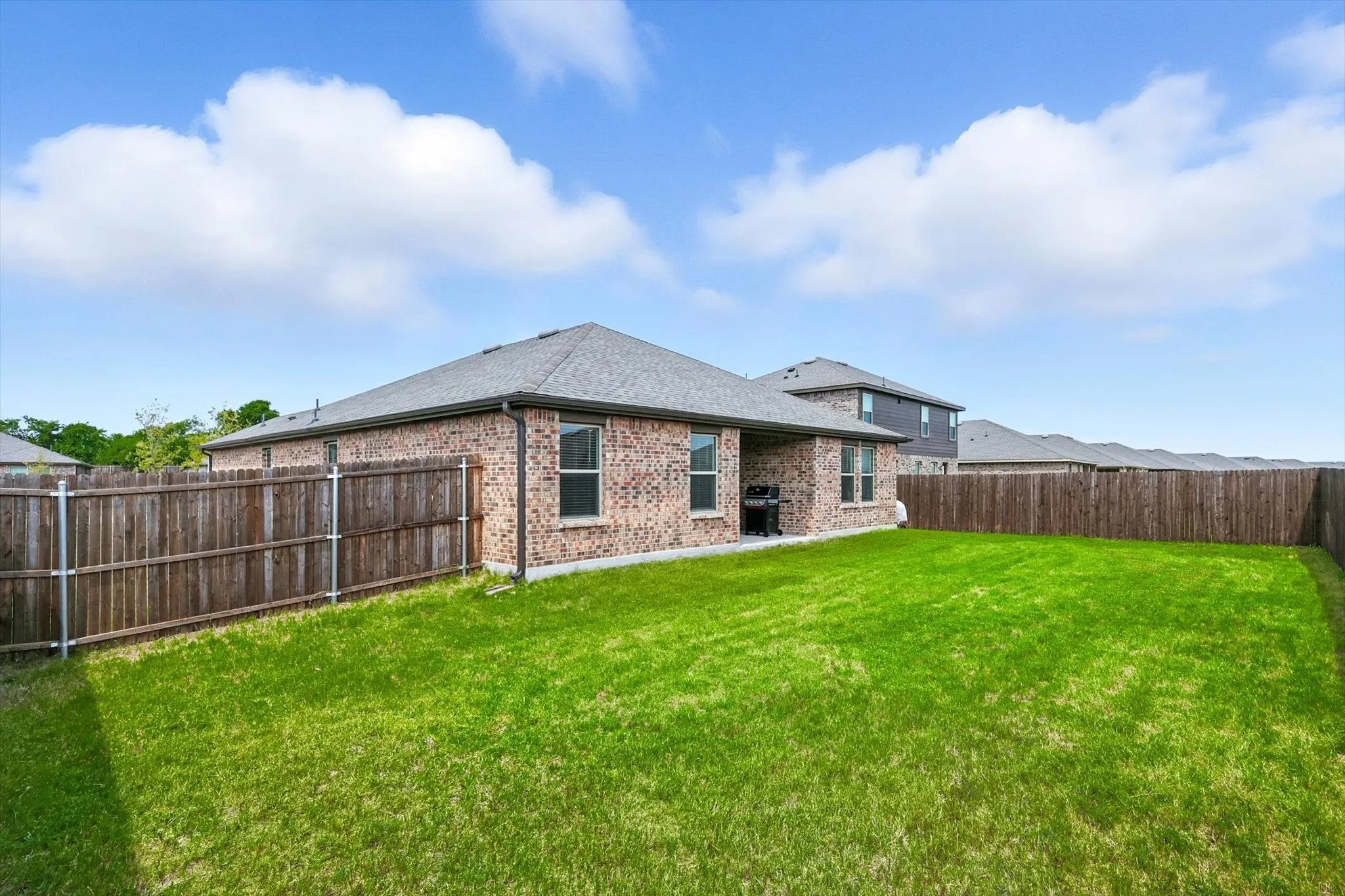 Expansive fenced yard with a manicured lawn, brick exterior, and a shingled roof