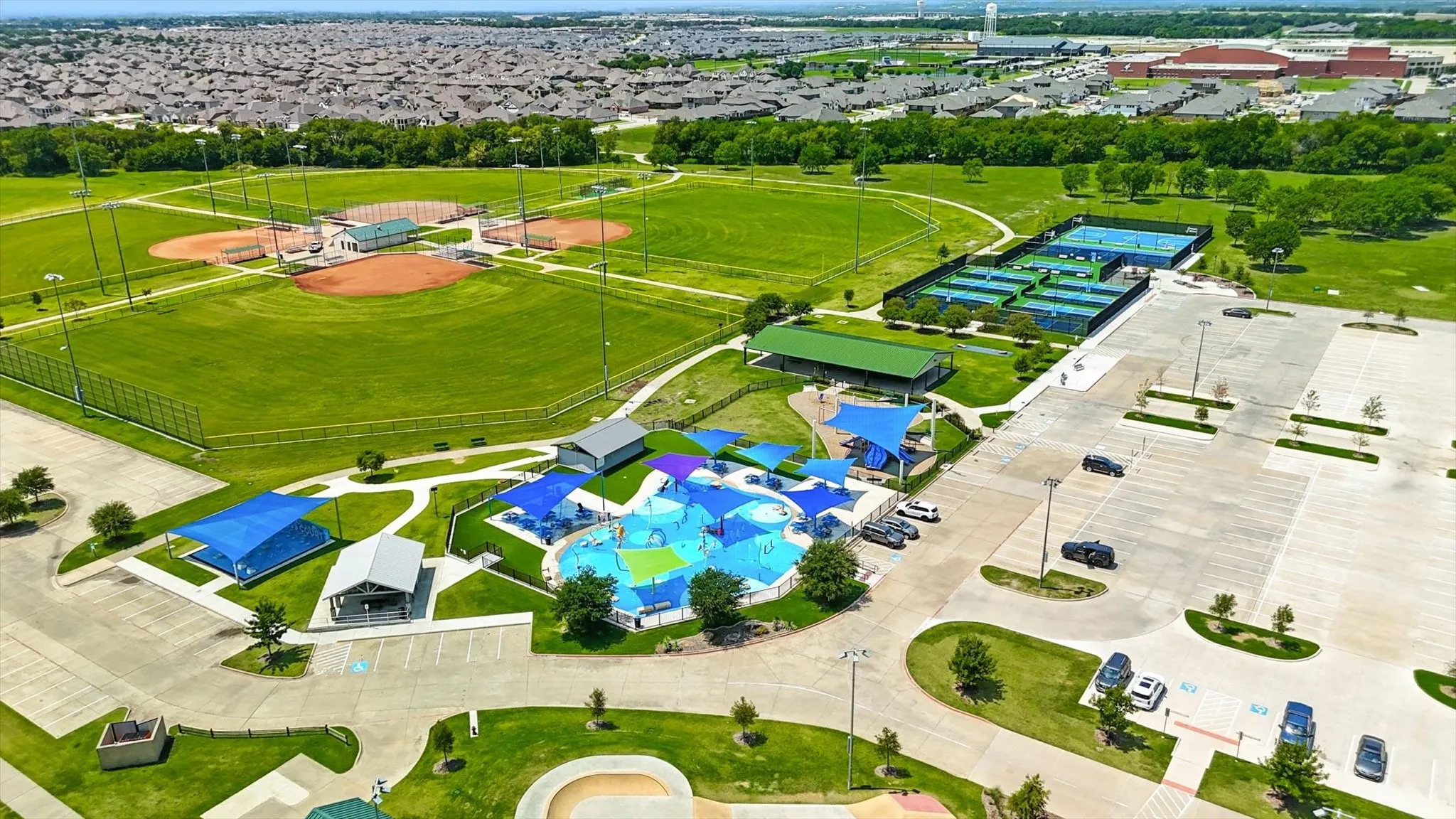 Expansive recreational area featuring multiple baseball fields, a water play park with shade structures, and several tennis courts