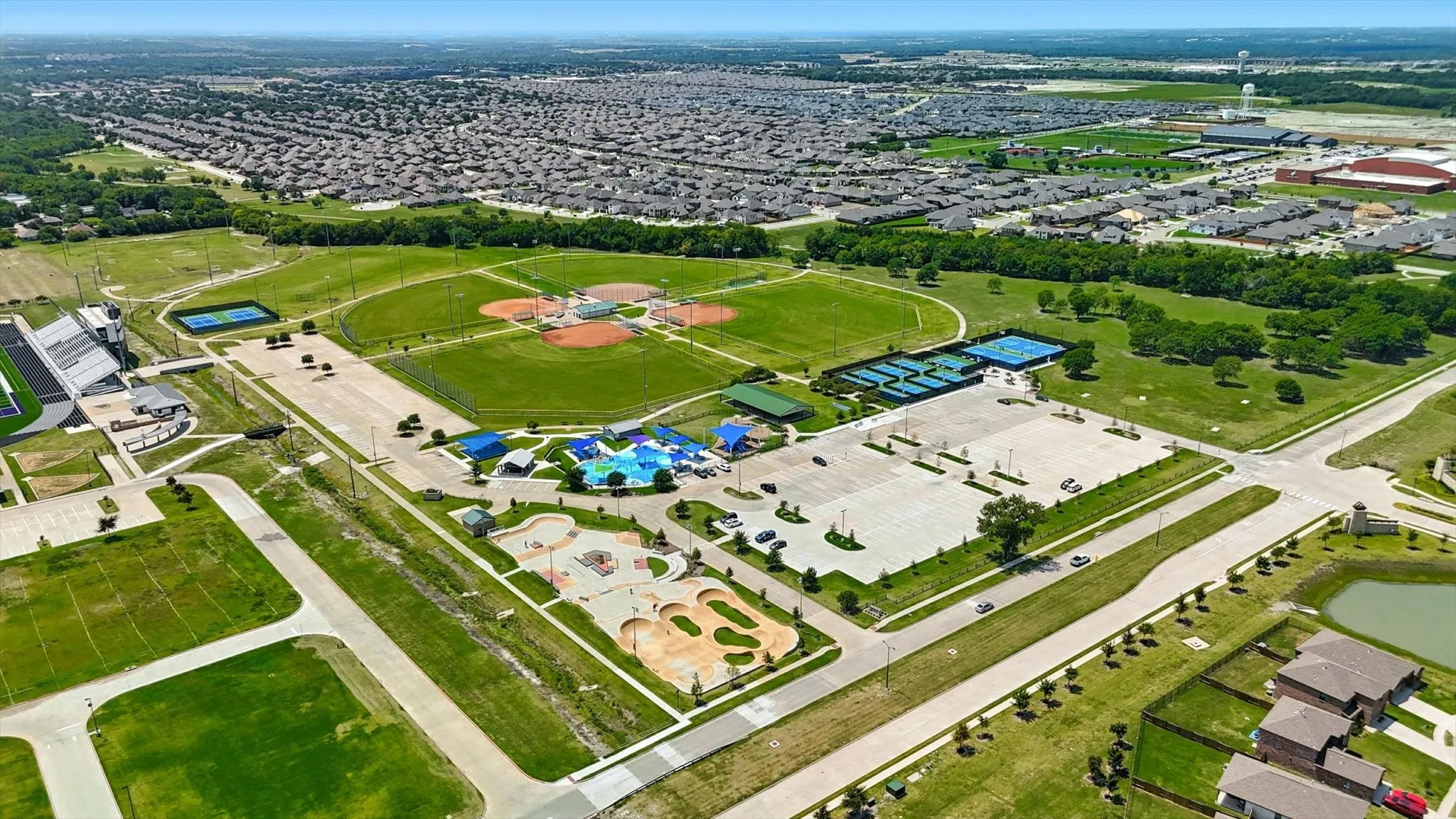 Expansive community park featuring multiple baseball diamonds, tennis courts, a skate park, and a water play area