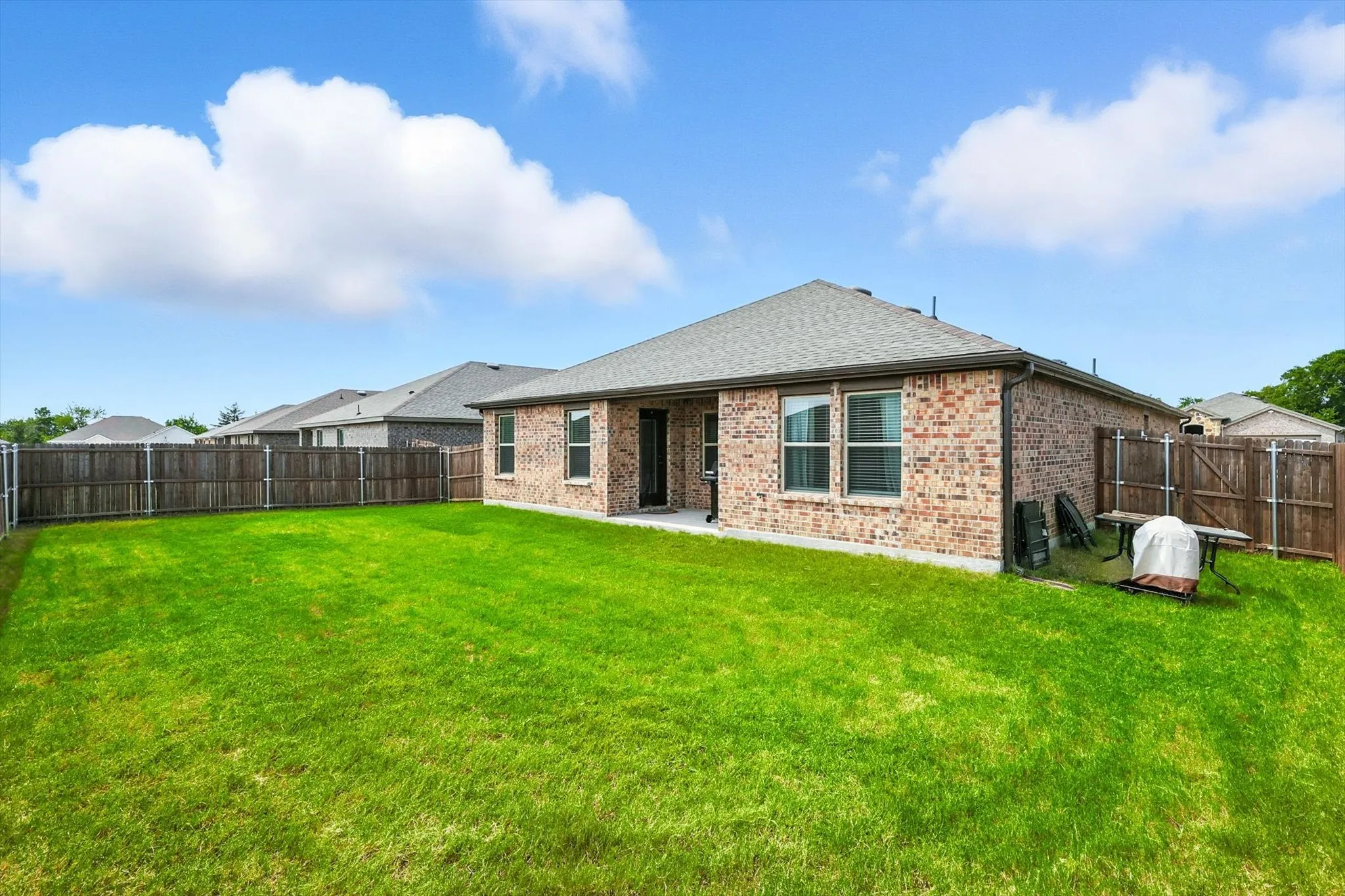 Expansive green lawn with a full privacy fence and a brick exterior