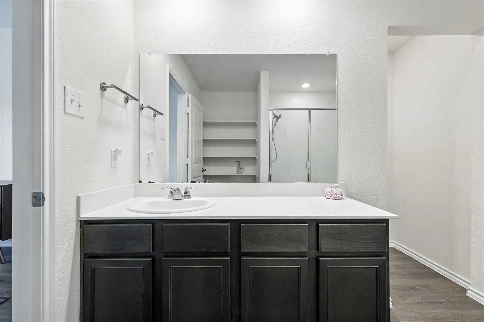 Vanity with a white countertop and dark wood-finish cabinetry, featuring an integrated sink, polished chrome faucet, and rectangular wall-mounted mirror