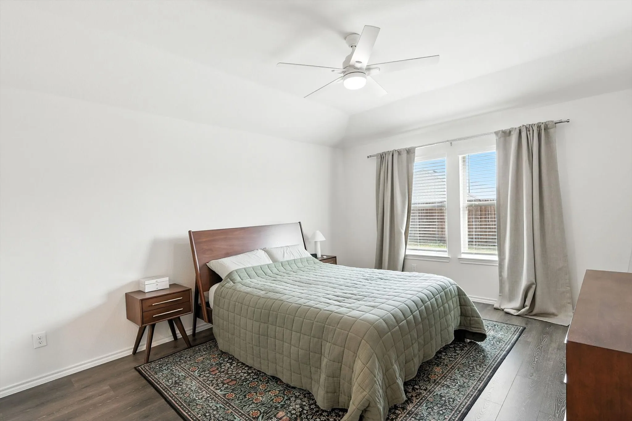 Vaulted ceiling with a ceiling fan, dual windows with blinds, wood-finish flooring, and white walls