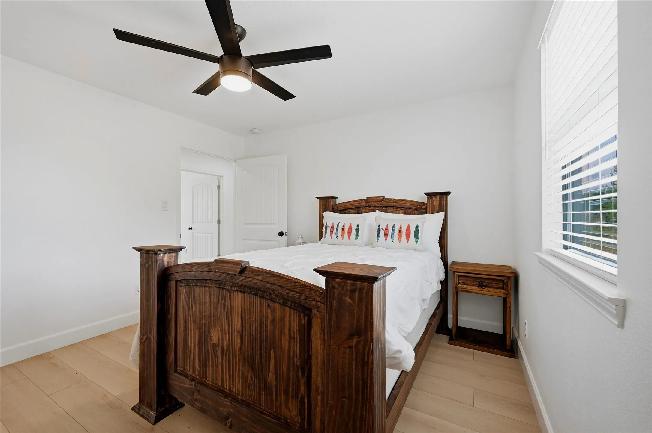 Light wood-finish flooring, white walls, and a ceiling fan with integrated lighting