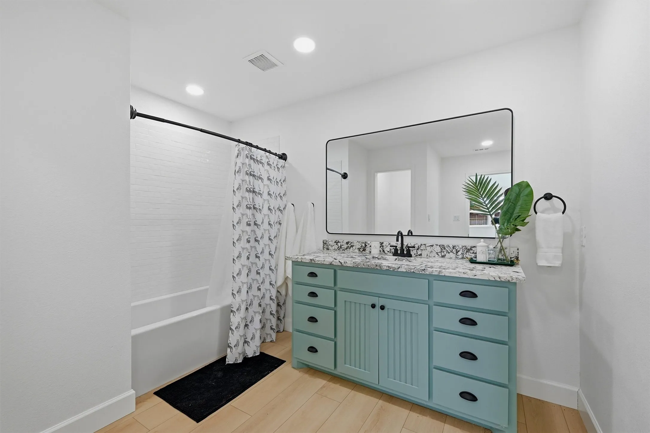 White subway tile shower surround with a built-in tub, blue vanity with black hardware, and a large rectangular mirror