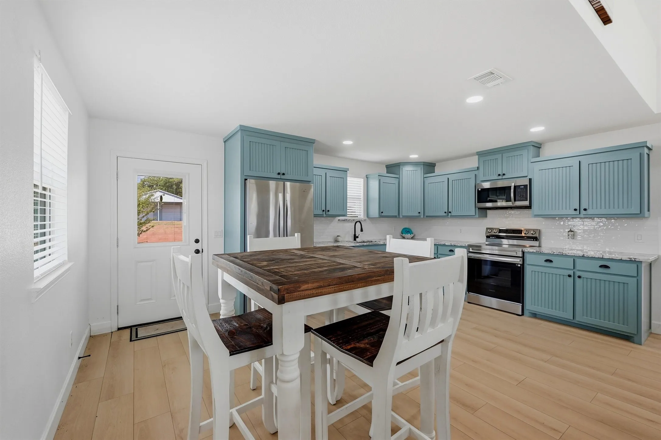 Open-concept kitchen featuring wood-finish flooring, light blue cabinetry, stainless steel appliances, and recessed lighting
