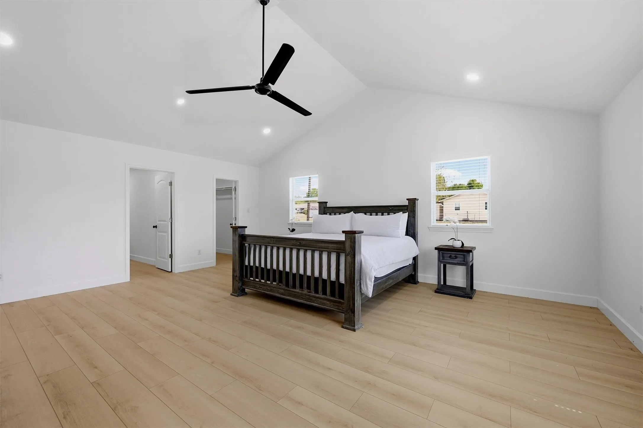 Vaulted ceiling with recessed lighting and a ceiling fan, light wood-finish flooring, and two windows