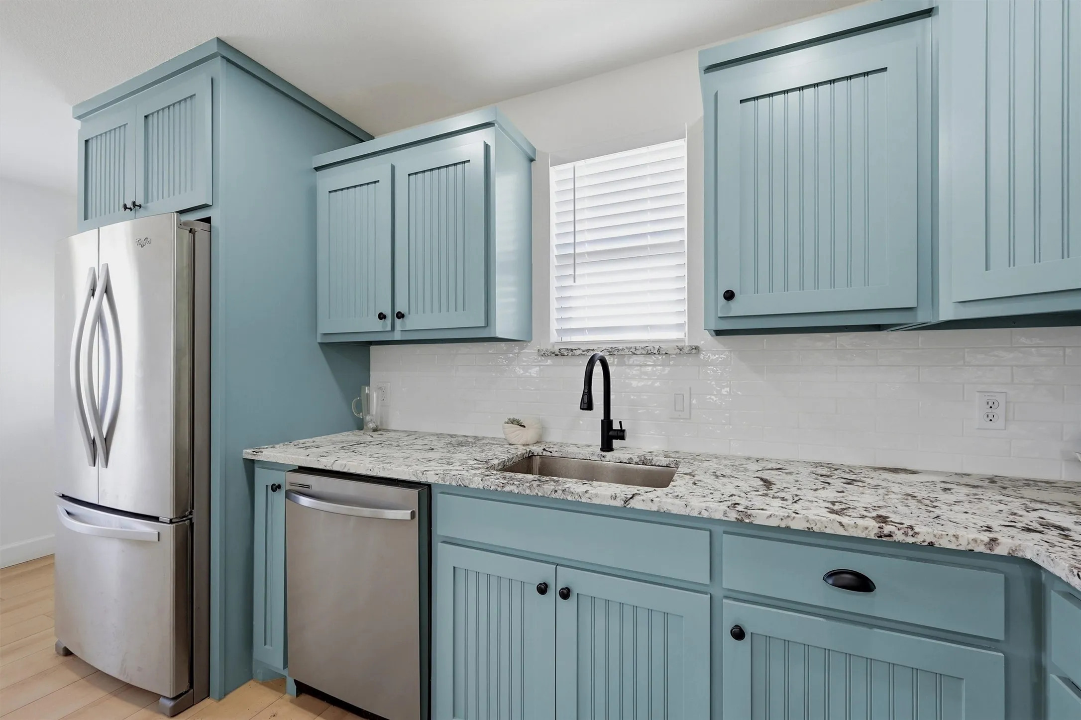 Custom beadboard cabinetry, stainless steel appliances, granite-style countertops, white subway tile backsplash, and a matte black gooseneck faucet