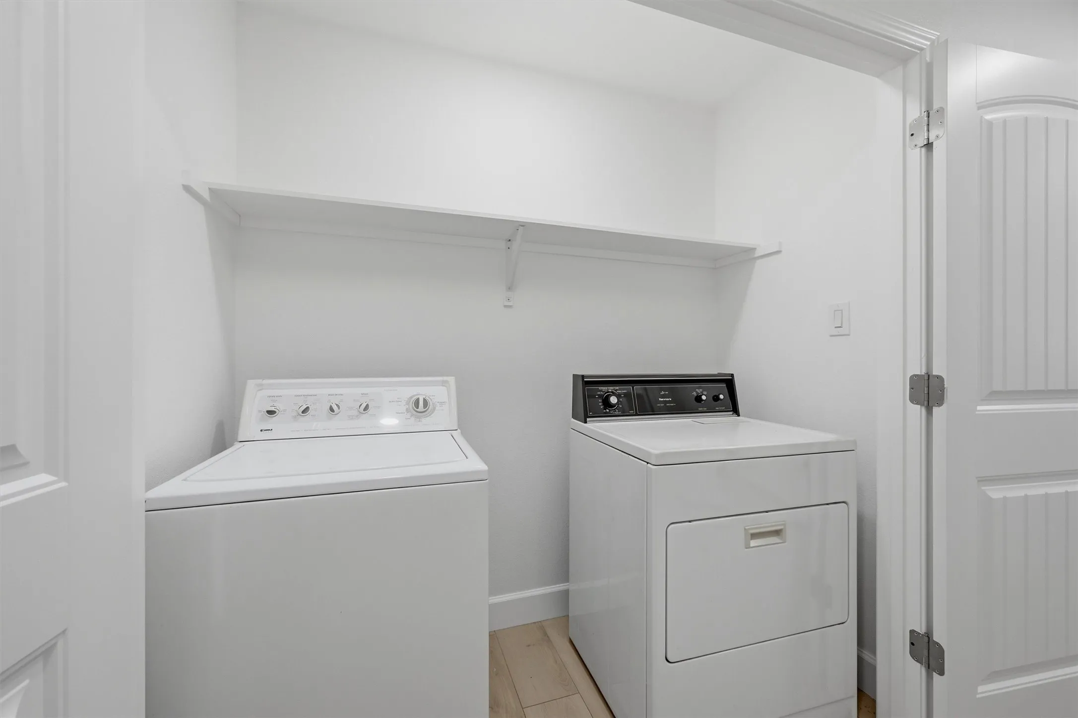 Dedicated laundry area featuring a washer, dryer, built-in shelving, wood-finish flooring, and a paneled door